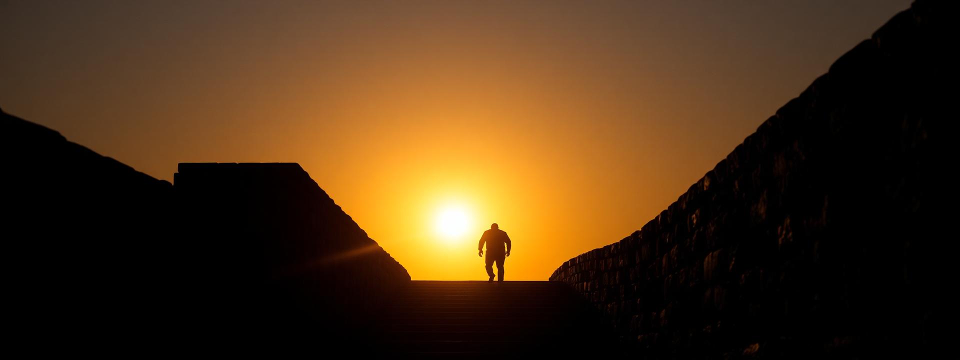 Silhueta de homem subindo escadaria em direção ao horizonte dourado ao amanhecer