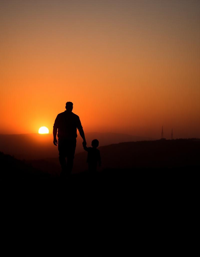 Silhueta de pai caminhando com duas crianças ao pôr do sol